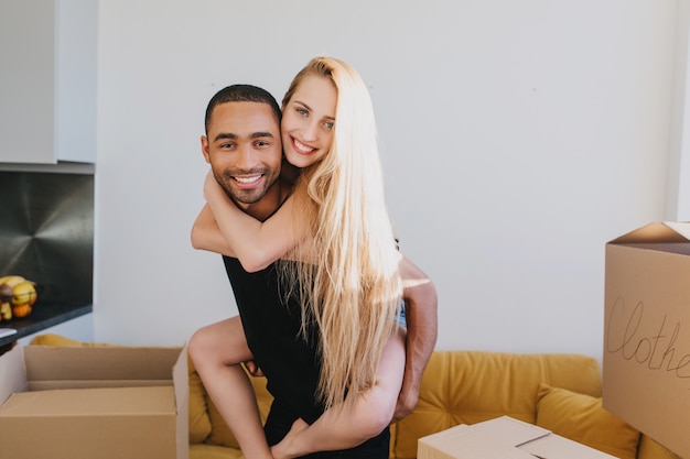 Close-upportret van paar dat pret in nieuw huis, huis, appartement, net is ingetrokken, jonge man en vrouw verliefd knuffelen rond dozen in kamer, meisje zittend op de rug van de man.