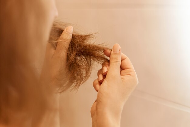 Close-upportret van vrouwenhanden die droog beschadigd haar houden, die trichologieprobleem hebben.