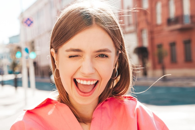 Gratis foto closeup portret van jonge mooie lachende hipster vrouw in trendy zomerkleren. sexy zorgeloze vrouw die zich voordeed op de straat achtergrond bij zonsondergang. positief model buitenshuis.blij en vrolijk.winks