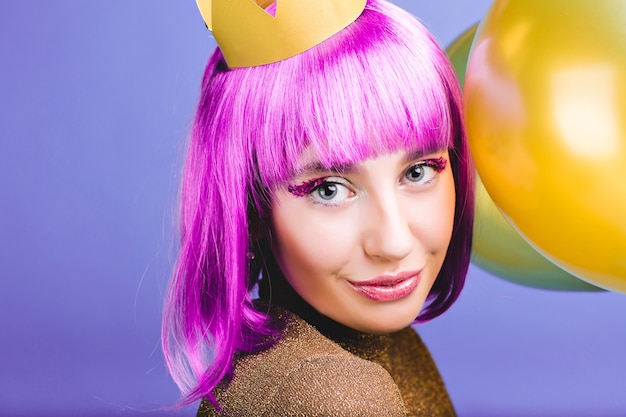 Closeup portret verbazingwekkende vrolijke jonge vrouw met gesneden paars haar, gouden kroon en ballonnen carnaval, nieuwjaarsfeest vieren. Charmante glimlach, make-up met tinsels, geluk.