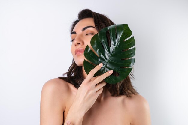 Closeup schoonheidsportret van een topless vrouw met perfecte huid en natuurlijke make-up met monsterapalmblad