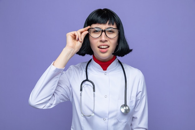 Clueless jong mooi Kaukasisch meisje met optische bril die artsenuniform met stethoscoop draagt