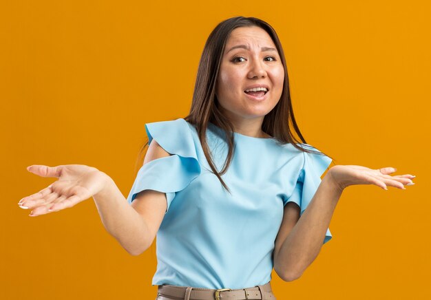 Clueless jonge aziatische vrouw die naar de voorkant kijkt met lege handen geïsoleerd op een oranje muur