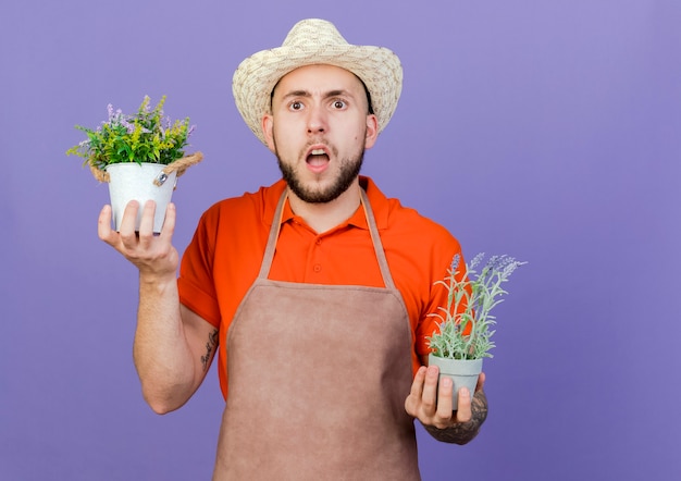 Clueless mannelijke tuinman die een tuinhoed draagt, houdt bloempotten vast