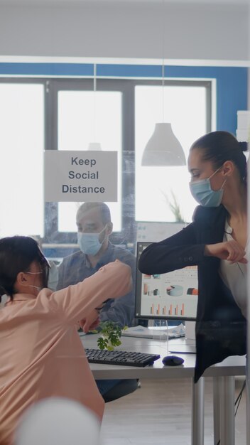 Collega's die de elleboog aanraken om infectie te voorkomen met een coronavirus business team dat een medisch gezichtsmasker draagt...