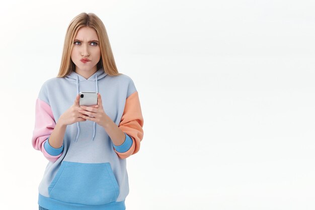 Communicatie, technologie en online concept. Verbijsterd en nadenkend jong blond meisje dat denkt hoe te antwoorden op riskante tekst in dating-app