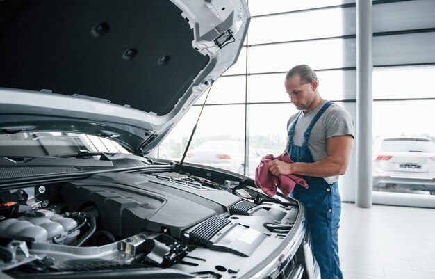 Concentreren op het werk. Man in blauw uniform werkt met kapotte auto. Reparaties maken