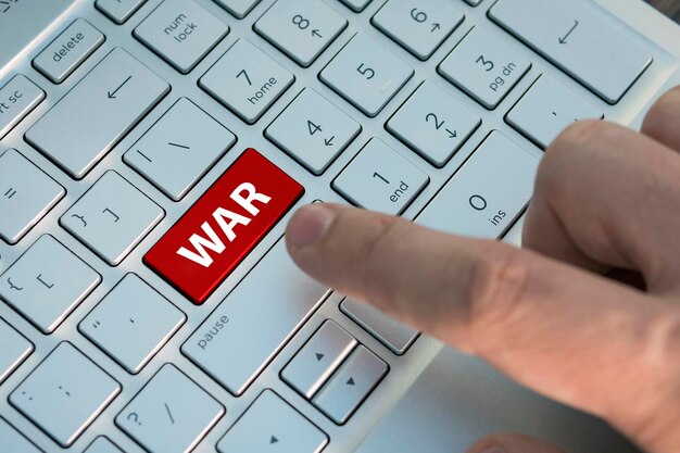 Concept, conceptie, idee, visie, begrip begin van de derde wereldoorlog. een mannelijke vinger drukt op een kleurenknop op een grijs zilveren toetsenbord van een moderne laptop. knop met inscriptie close-up.