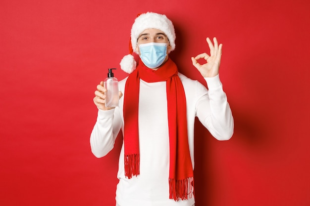 Concept van covid kerst en feestdagen tijdens pandemische aantrekkelijke man in kerstmuts en medisch masker...