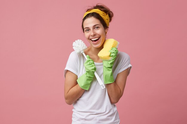 Concept van hygiëne, schoonmaak, netheid, huishoudelijk werk en huishouding. portret van terloops geklede jonge blanke huisvrouw toiletborstel en spons te houden tijdens het huishouden