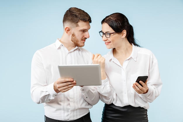 Concept van partnerschap in zaken. Jonge emotionele man en vrouw tegen blauwe achtergrond bij studio. Menselijke emoties en partnerschap concept