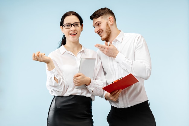 Concept van partnerschap in zaken. Jonge gelukkige glimlachende man en vrouw die zich tegen blauwe achtergrond bij studio bevinden