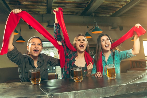 Gratis foto concept van sport, mensen, vrije tijd, vriendschap, entertainment - gelukkige vrouwelijke voetbalfans of goede jonge vrienden die bier drinken, de overwinning vieren in de bar of pub. menselijke positieve emoties concept