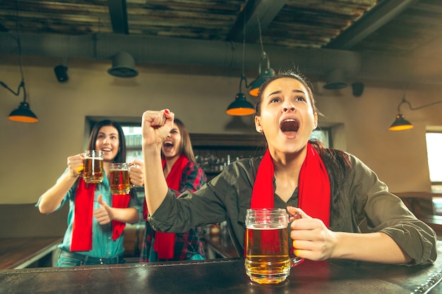 Concept van sport, mensen, vrije tijd, vriendschap, entertainment - gelukkige vrouwelijke voetbalfans of goede jonge vrienden die bier drinken, de overwinning vieren in de bar of pub. Menselijke positieve emoties concept