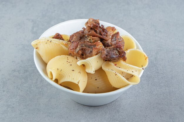 Conchiglie pasta met gegrilde kip in witte kom.