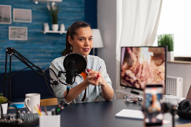 Content creator streaming make-up review voor social media kanaal. Populaire influencer die productaanbevelingsvideo opneemt met smartphone en microfoon voor vlog in thuisstudio.