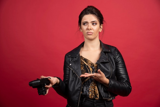 Cool meisje in zwart leren jasje met haar professionele camera vast en kijkt ontevreden over haar fotogeschiedenis.