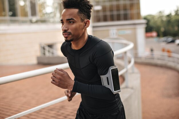 Coole donkerbruine man met donkere huidskleur in t-shirt met lange mouwen en korte broek die naar boven rent Jonge man met baard die aan het trainen is