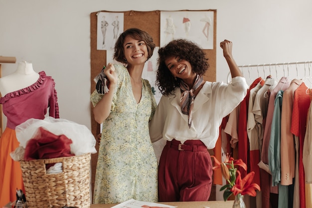 Coole jonge dames poseren in de buurt van etalagepop in kantoor van modeontwerper