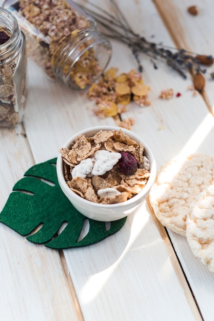 Cornflakes in kom dichtbij gemorste kruik granola en rijstcrackers op houten achtergrond