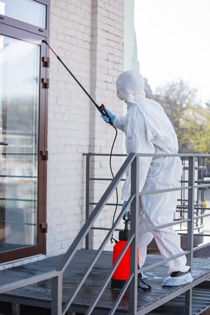 Coronavirus Pandemic. Een ontsmettingsmiddel in een beschermend pak en masker spuit ontsmettingsmiddelen in de kamer.