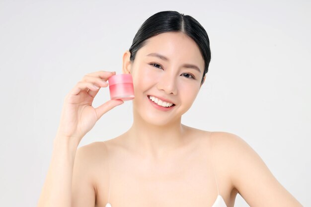 Cosmetische gezichtscrème close-up schoonheid gezicht Aziatische vrouw met frisse schone huid met gezichtscrème fles geïsoleerd op wit Schoonheid en huidverzorging Concept