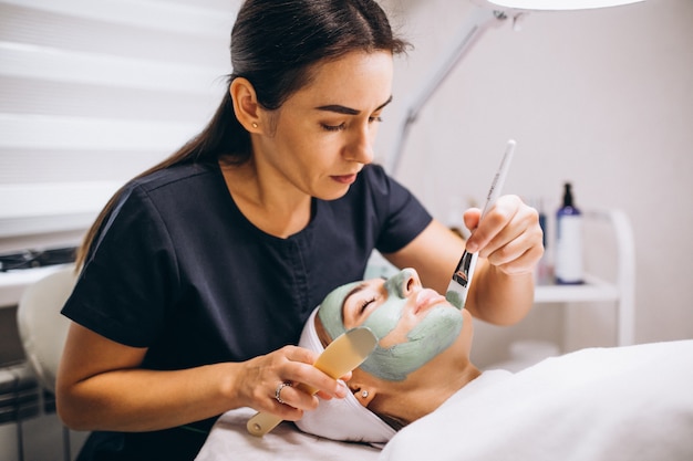 Cosmetologist die masker op een gezicht van cliënt toepast in een schoonheidssalon