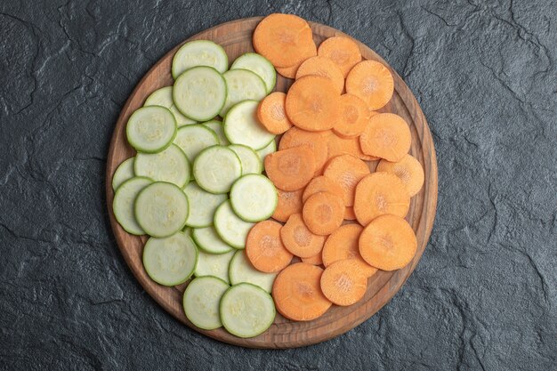 Courgette en wortelplakken in houten plaat op zwarte achtergrond. Hoge kwaliteit foto