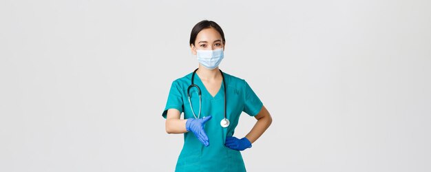Covid-19, coronavirusziekte, concept van gezondheidswerkers. Zelfverzekerde jonge aziatische vrouwelijke arts, arts in scrubs en medisch masker, handschoenen, strek hand uit voor handdruk, groet patiënt