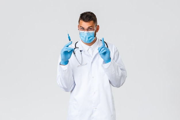 Covid-19, gezondheidswerkers, pandemie en virusconcept. Jonge knappe dokter met medisch masker en handschoenen, scrubs met spuit met coronavirusvaccin, aanbevelen vaccineren en schieten