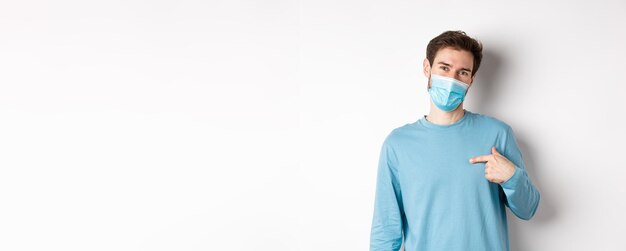 Covid gezondheids- en quarantaineconcept glimlachende blanke man met medisch masker wijzend naar zichzelf vrijwillig