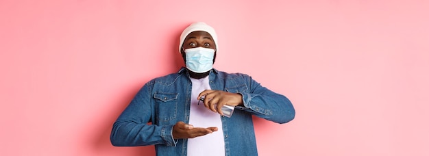 Gratis foto covid-levensstijl en lockdown-concept glimlachende afro-amerikaanse man in gezichtsmasker die handen schoonmaakt met sa