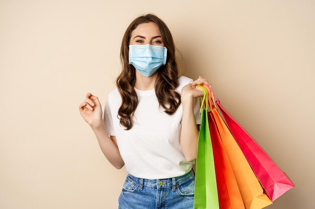 Covid pandemie en lifestyle concept jonge vrouw poseren in medisch gezichtsmasker met boodschappentassen van...