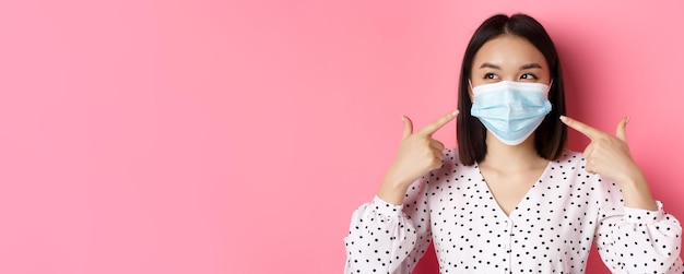 Covid pandemie en lifestyle concept kawaii aziatisch meisje wijzende vingers naar haar gezichtsmasker dat pre draagt