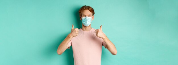 Covid pandemie en lifestyle concept vrolijke roodharige man met medisch masker duimen omhoog in app