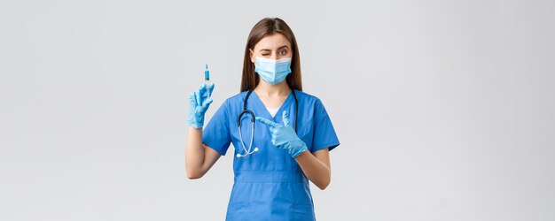 Covid19 die virusgezondheidswerkers en quarantaineconcept voorkomt Leuke vrouwelijke verpleegster of arts in blauwe scrubs medisch masker PPE-aanwijsspuit gevuld met coronavirusvaccin