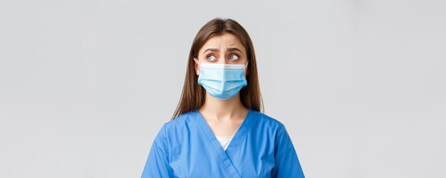 Covid19 die virusgezondheidswerkers en quarantaineconcept voorkomt Sceptische verontruste vrouwelijke verpleegster of arts in blauwe scrubs medisch masker kijkt linkerbovenhoek onzeker of verbaasd
