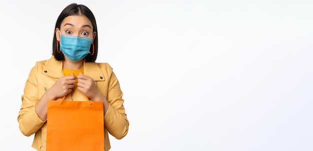 Covid19 en winkelconcept Jonge Aziatische stijlvolle vrouw met een medisch gezichtsmasker met een boodschappentas die in winkelcentra gaat tijdens pandemische witte achtergrond