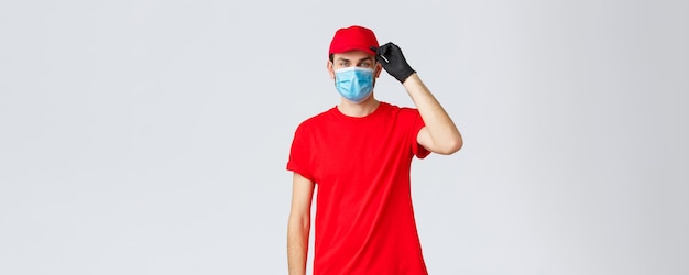 Covid19 zelfquarantaine online winkel- en verzendconcept Vriendelijke bezorger die de klant groet terwijl hij boodschappenpakketten aan de deur bezorgt Zelfquarantainebestellingen dragen een medisch masker en handschoenen