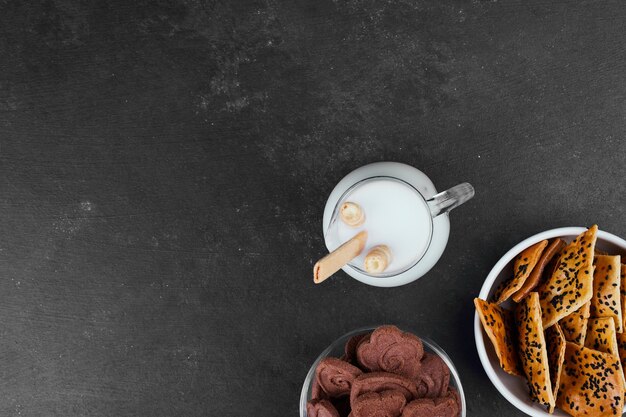 Crackers met een glas melk op zwart, bovenaanzicht.