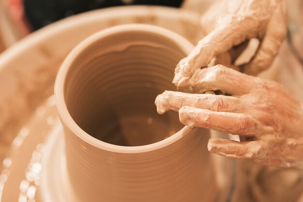 Craftswoman vormt de aarden pot met zijn handen op een aardewerkwiel