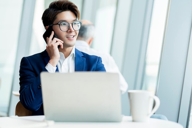 Creatieve bureau slimme bril Aziatische mannelijke formele doek gesprek met smartphone freelance werken met laptop bij coworking gebied kantoorruimte met frisheid met wazige kantoorachtergrond