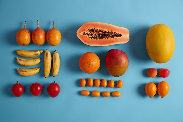 Creatieve lay-out van sappige tropische vruchten op blauwe achtergrond. rijpe bananen, rode fortunella, sinaasappels, perziken, de helft van papaja, cumquat. exotisch fruit voor uw gezonde voeding. schoon eten, vitamines