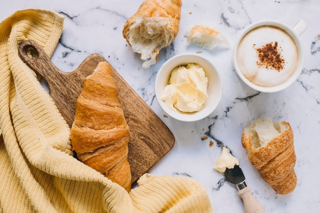 Croissant; boter en koffiekopje op marmeren blad met geel servet