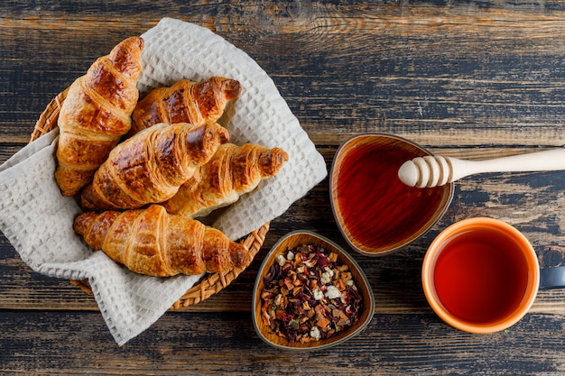 Croissant in een mand met honing, beer, thee, gedroogde kruiden plat lag op een houten tafel