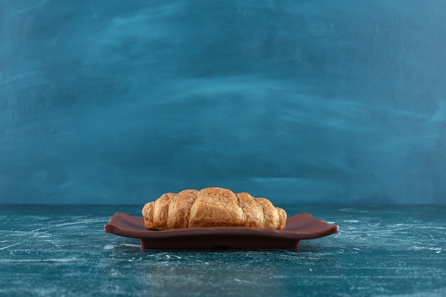 Croissant op een bruin bord, op de blauwe tafel.