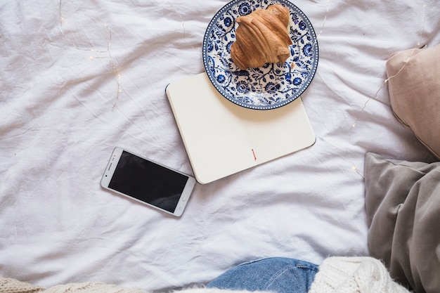 Croissant op plaat dichtbij notitieboekje en smartphone