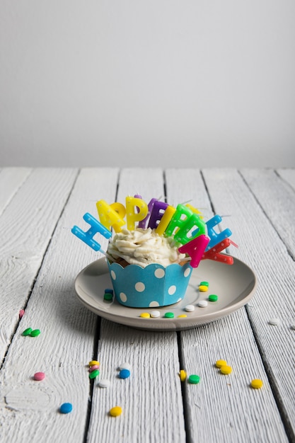 Cupcake met kleurrijke verjaardagskaarsen en suikergoed op houten geweven lijst