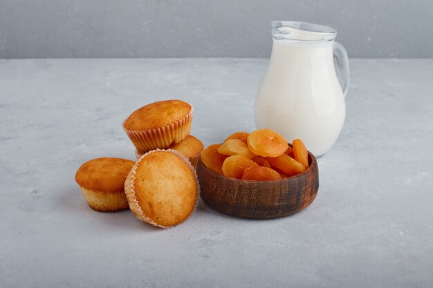 Cupcakes en droge abrikozen met een potje melk op een grijze achtergrond.