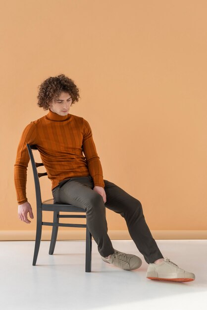 Curly haired man met bruine blouse poseren op stoel